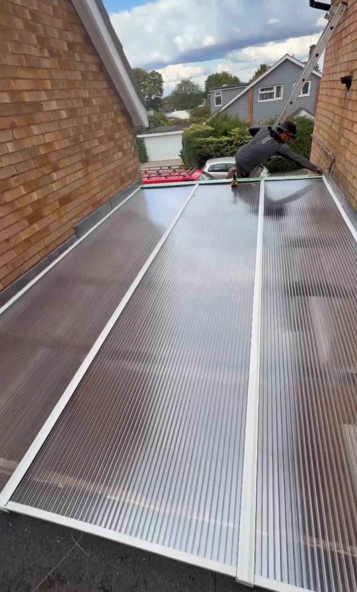 A roofer fitting clear multiwall sheets on a lean-to roof between two walls