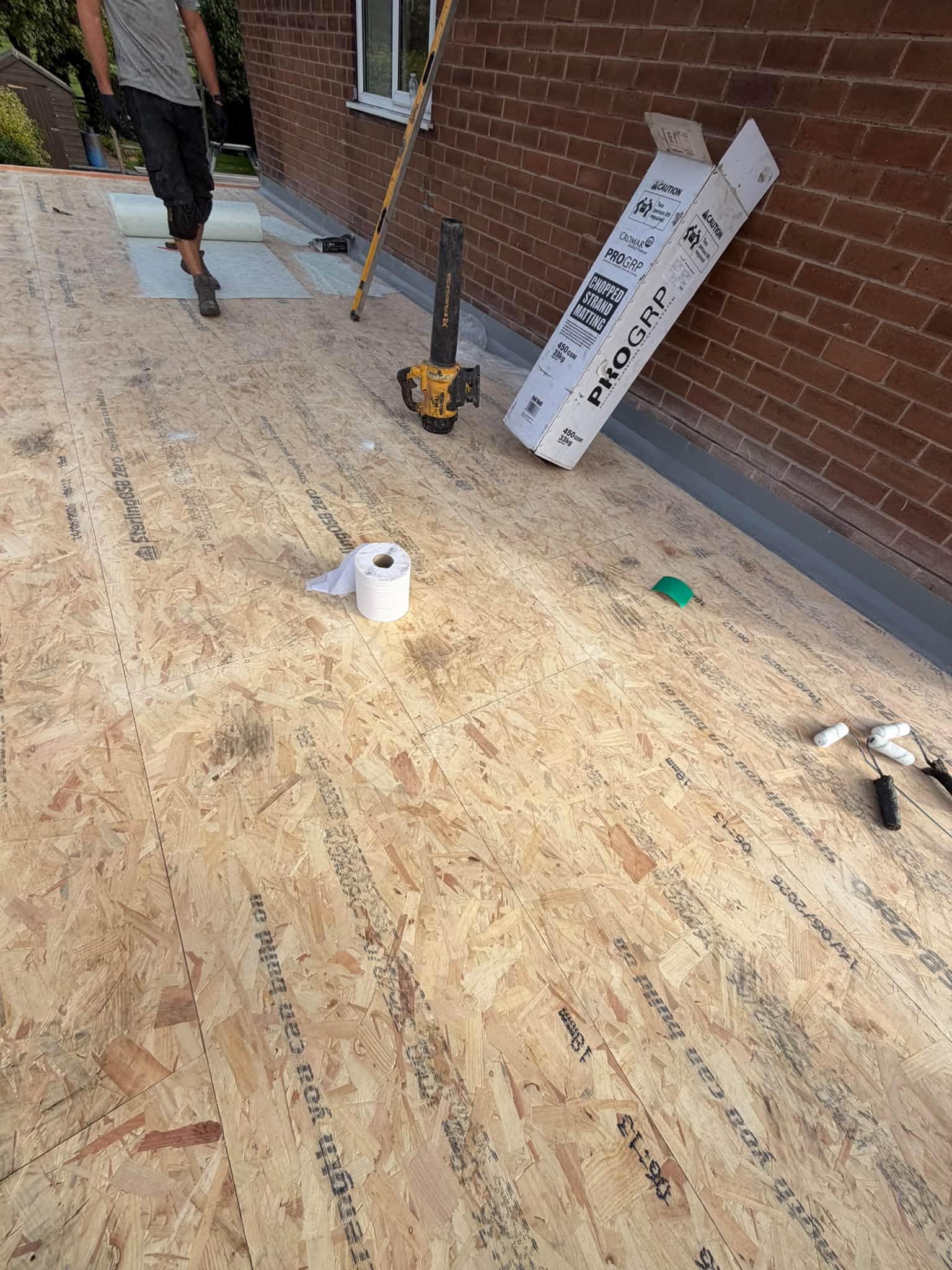 New timber deck boards being laid on a flat roof against a brick wall