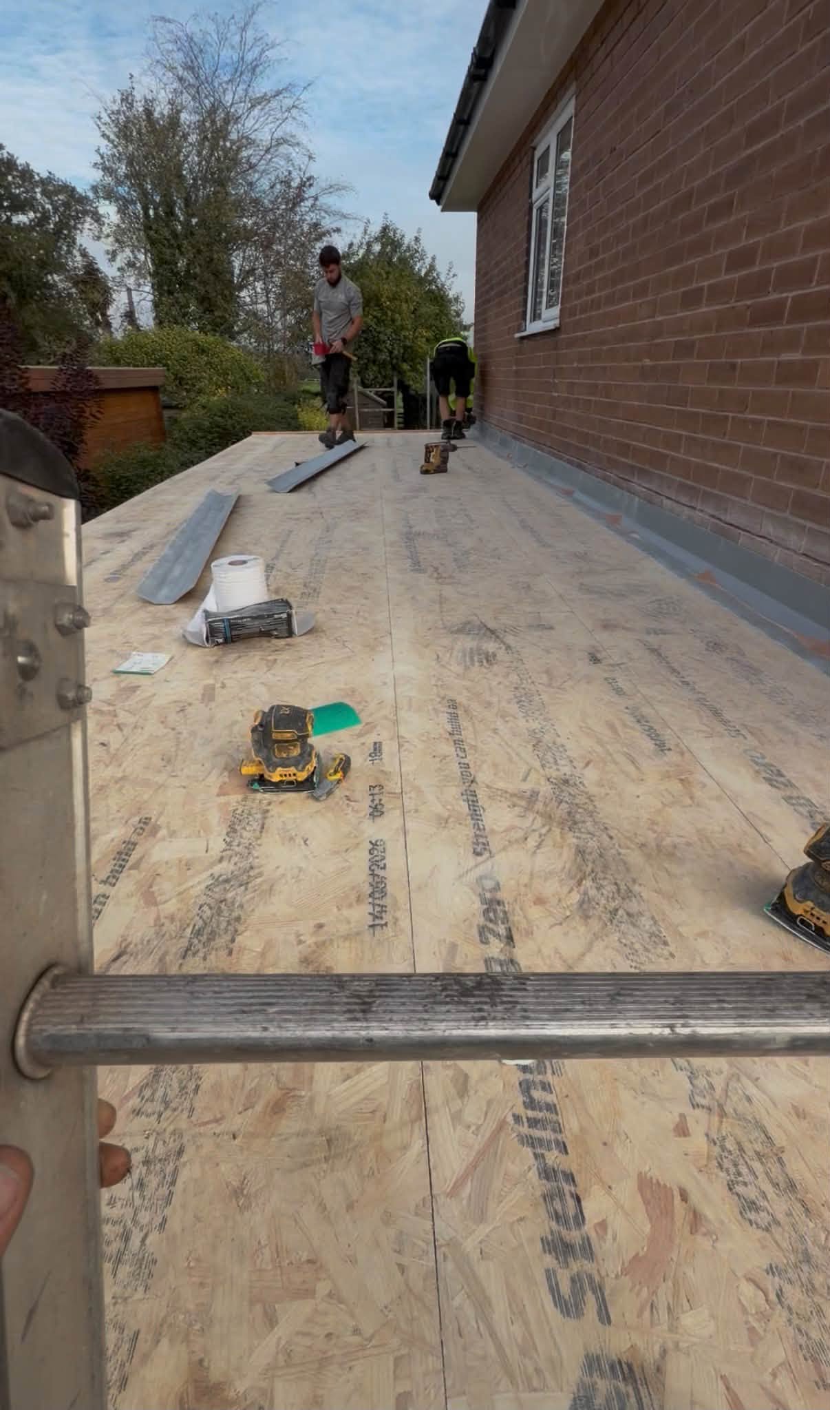 Two of the Scope Roofing team on a flat roof deck in progress, with scaffold along the edge