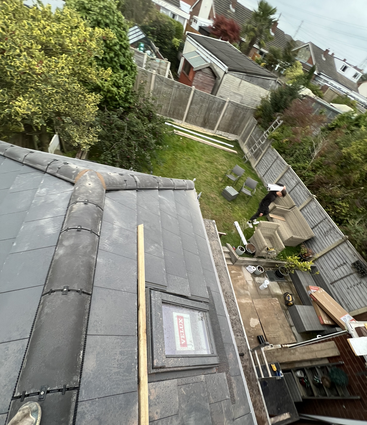 A newly tiled slate-grey roof with a dry ridge and a roof window, looking down onto a garden