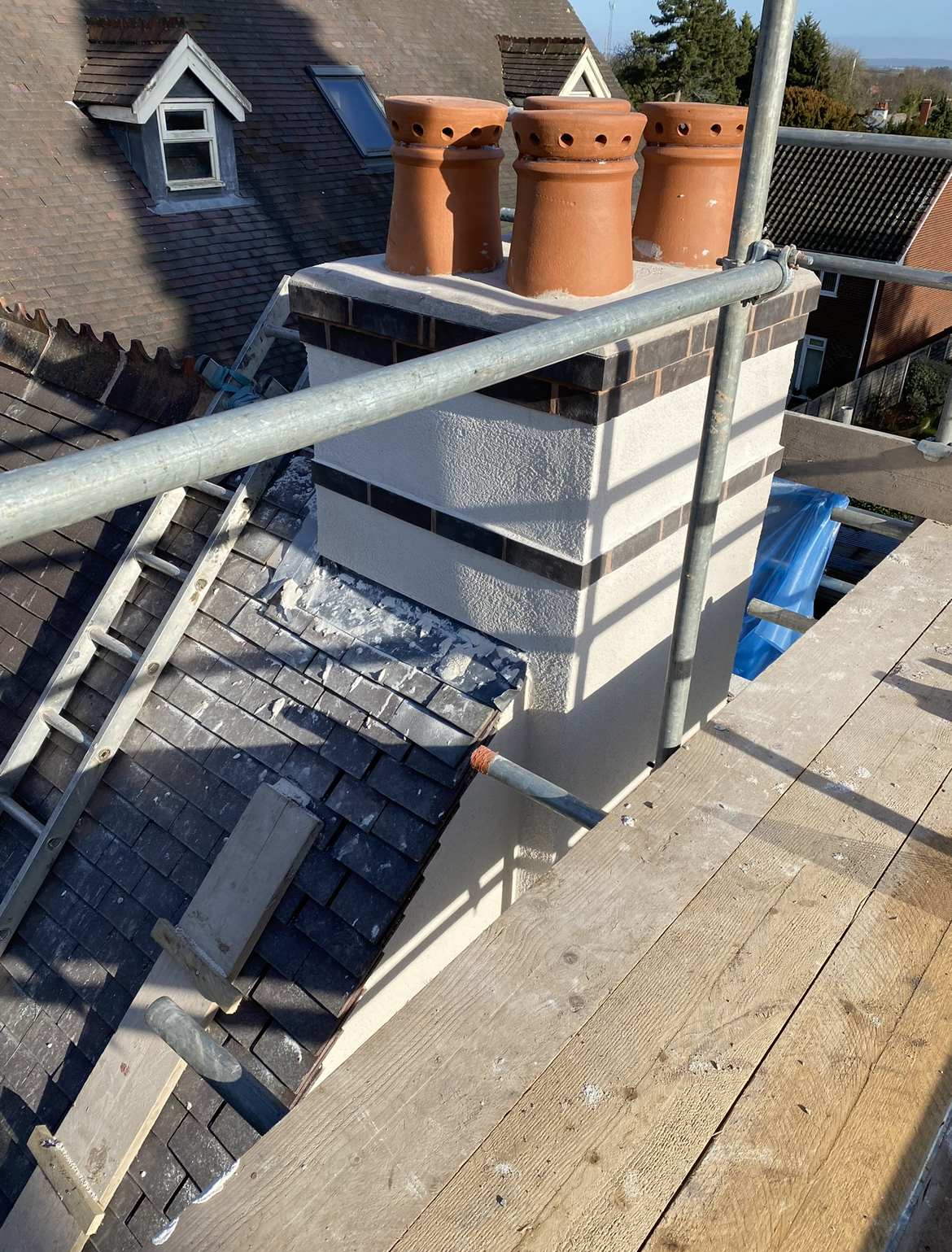 A rendered chimney stack with three clay pots, seen from the scaffold