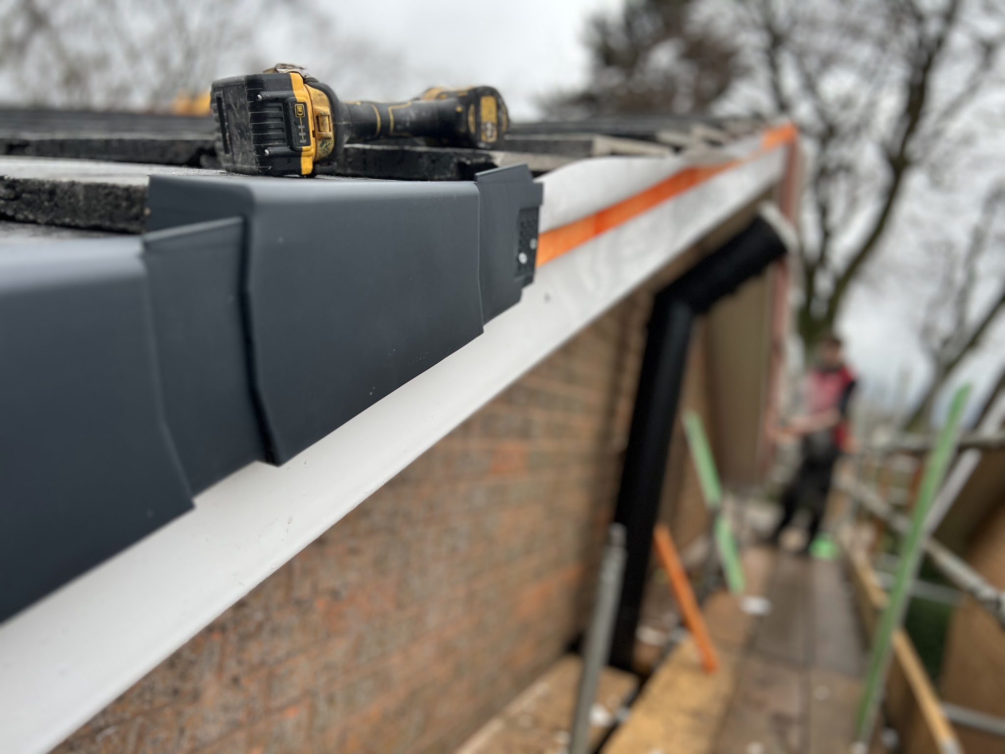 Close-up of a new dark grey roof edge trim on a white fascia, a drill resting on top